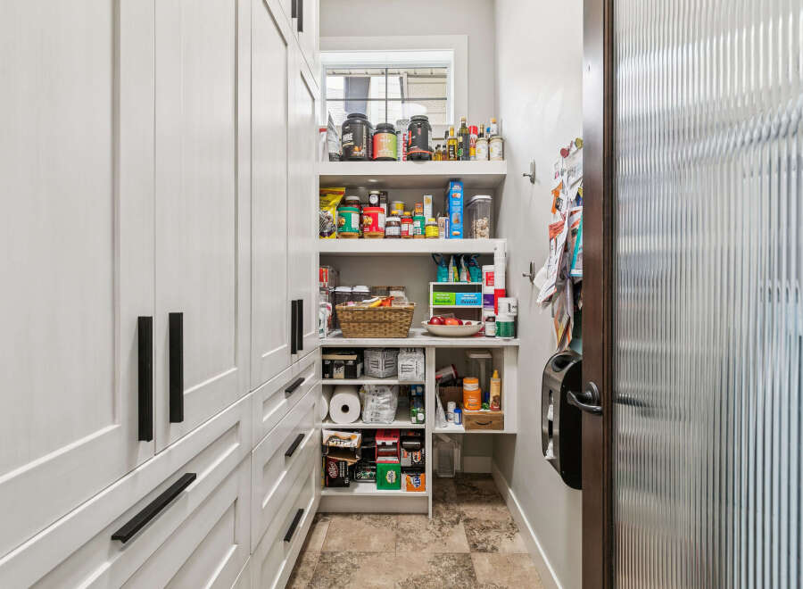 Discover ample storage in this well-organized pantry, featuring custom white cabinetry with sleek black hardware.