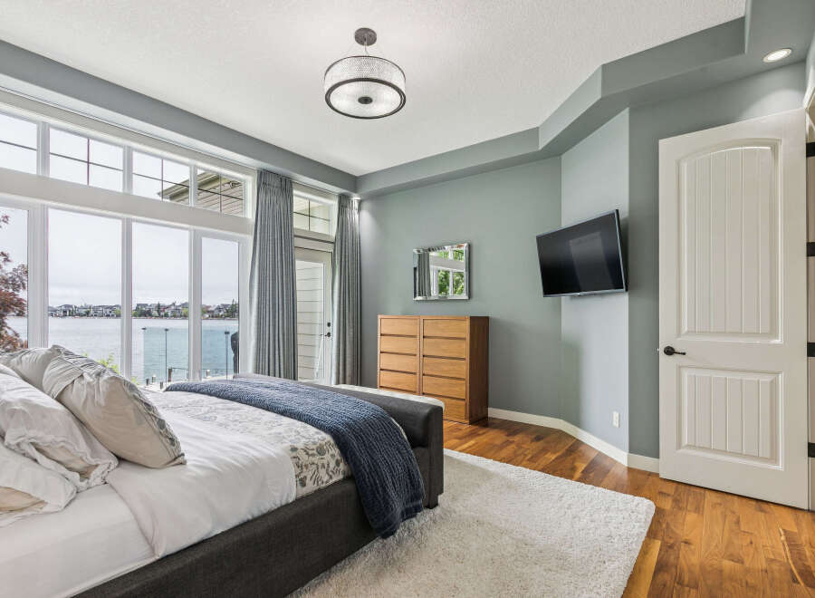 Experience luxurious waterfront living in this stunning master bedroom, featuring expansive windows that offer breathtaking lake views.