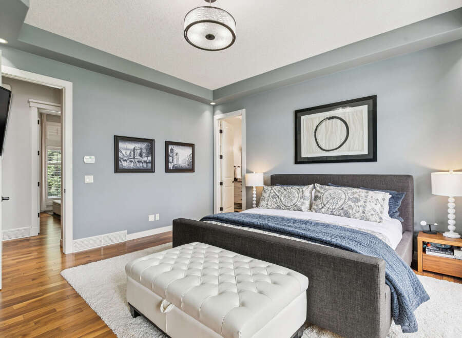 Experience ultimate comfort in this serene master bedroom, featuring a plush king-sized bed adorned with elegant patterned pillows and a cozy blue quilt.