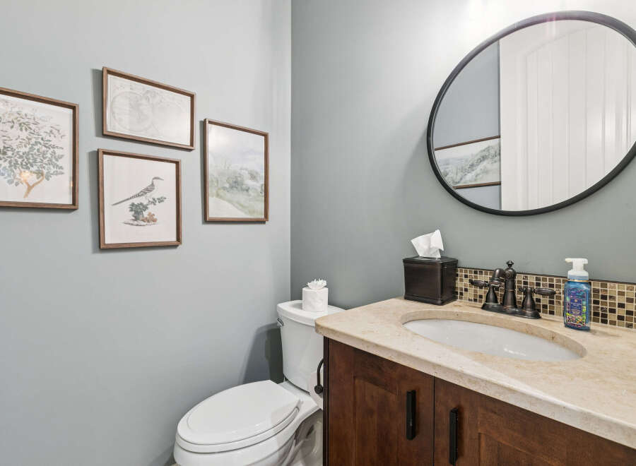 This powder room features a stylish vanity with a granite countertop and a dark wood cabinet, complemented by a mosaic tile backsplash.