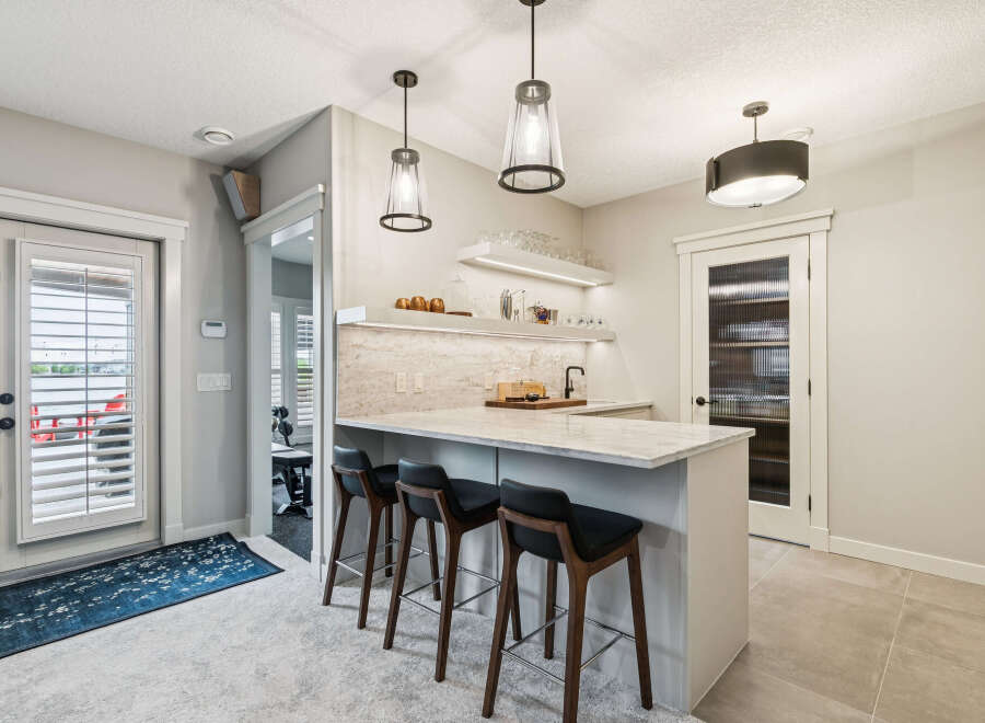 This modern basement features a stylish wet bar with a marble countertop, sleek pendant lighting, and ample shelving for glassware.