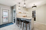 This modern basement features a stylish wet bar with a marble countertop, sleek pendant lighting, and ample shelving for glassware.