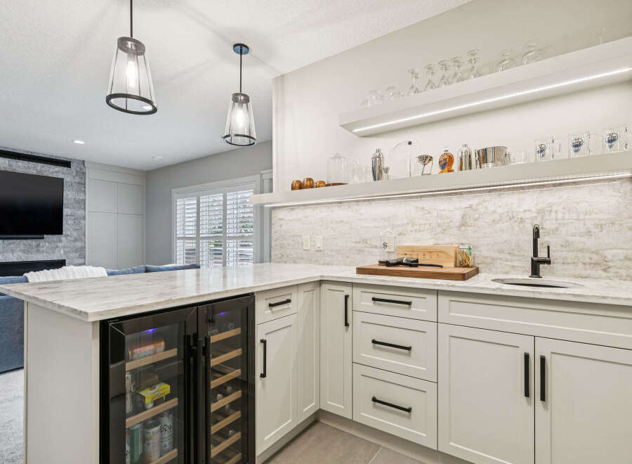 This modern basement bar features a sleek white cabinetry with marble countertops and a built-in wine fridge.