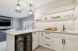 This modern basement bar features a sleek white cabinetry with marble countertops and a built-in wine fridge.