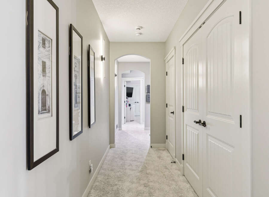 Step into this elegant hallway featuring a plush, neutral carpet and sophisticated wall sconces that cast a warm glow.
