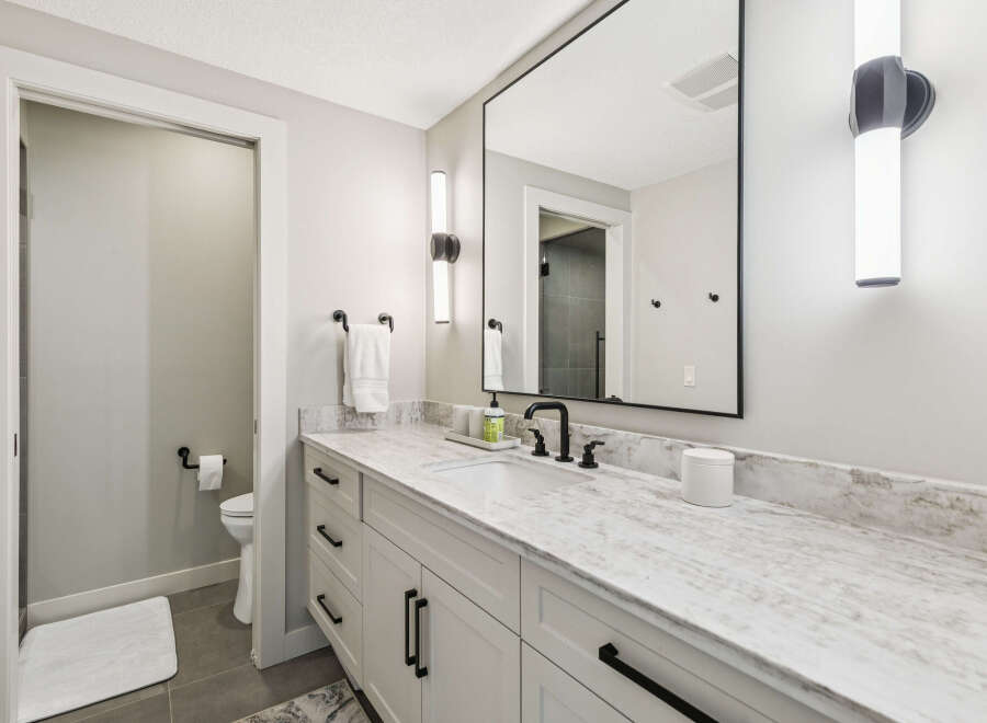This modern bathroom features a sleek white vanity with a stunning marble countertop and black hardware.