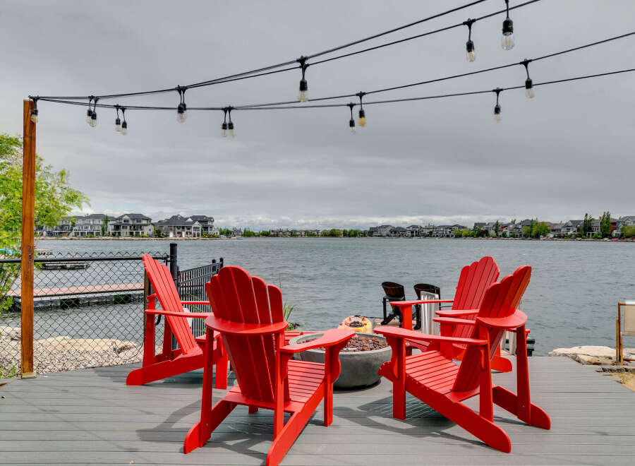 Enjoy breathtaking lake views from this stunning waterfront property, featuring a spacious deck with vibrant red Adirondack chairs perfect for relaxing.