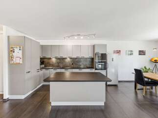 Discover this modern kitchen featuring sleek, light gray cabinetry and a spacious island with a dark countertop, perfect for meal preparation and casual dining.