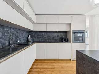 Experience modern luxury in this sleek kitchen, featuring high-gloss white cabinetry and a striking dark stone backsplash.