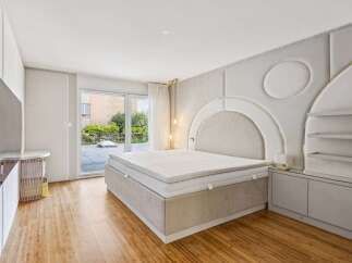 Experience modern luxury in this stunning bedroom featuring a king-size bed with a plush upholstered headboard and a unique geometric wall design.