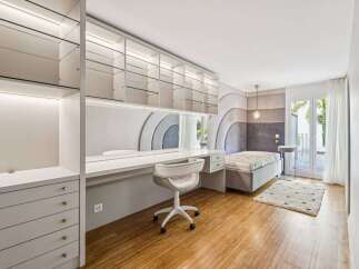 Discover this modern bedroom featuring a sleek white desk with integrated shelving and a comfortable white office chair.