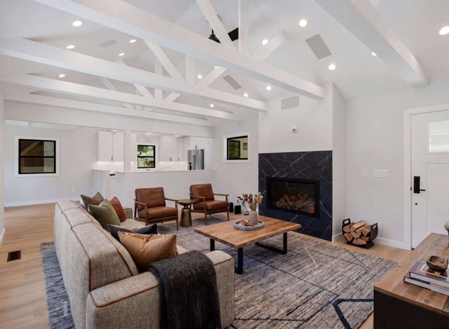 Experience modern living in this stunning living room, featuring a dramatic black marble fireplace and vaulted ceilings with exposed beams.