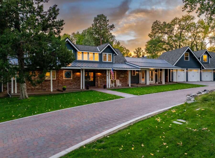 This stunning property features a beautiful brick and dark blue siding exterior, complemented by a metal roof and a welcoming front porch with rocking chairs.