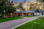 This stunning property features a beautiful brick and dark blue siding exterior, complemented by a metal roof and a welcoming front porch with rocking chairs.