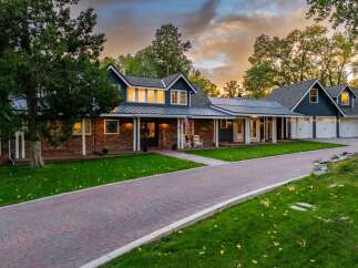 This stunning property features a beautiful brick and dark blue siding exterior, complemented by a metal roof and a welcoming front porch with rocking chairs.