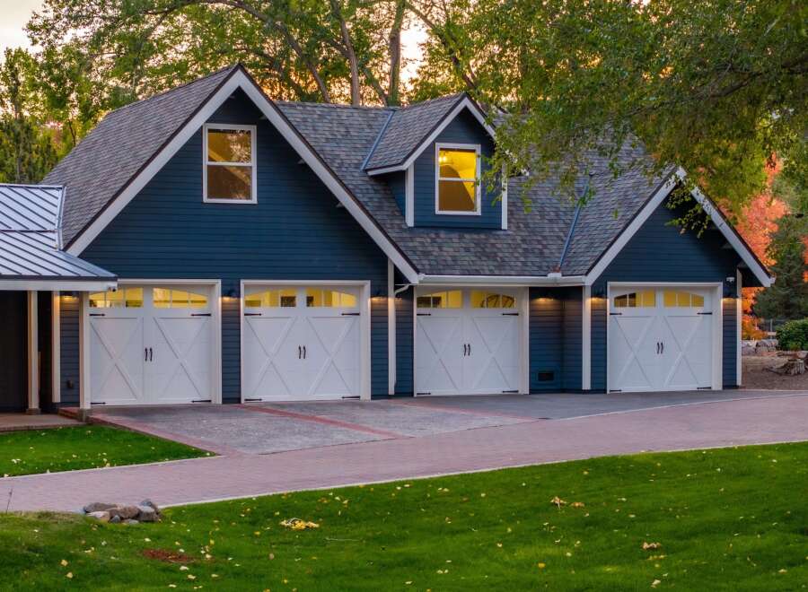 This stunning property features a spacious multi-car garage with classic white doors and dark hardware, set against a deep blue siding.