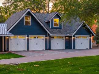 This stunning property features a spacious multi-car garage with classic white doors and dark hardware, set against a deep blue siding.