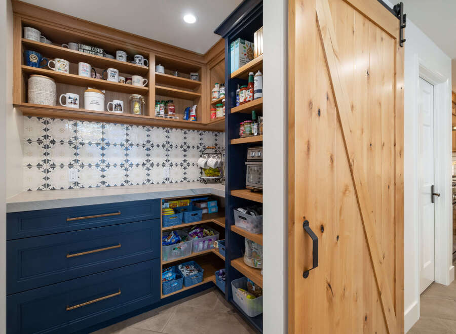 Discover the ultimate pantry organization with this beautifully designed space, featuring custom navy blue cabinetry and open shelving.