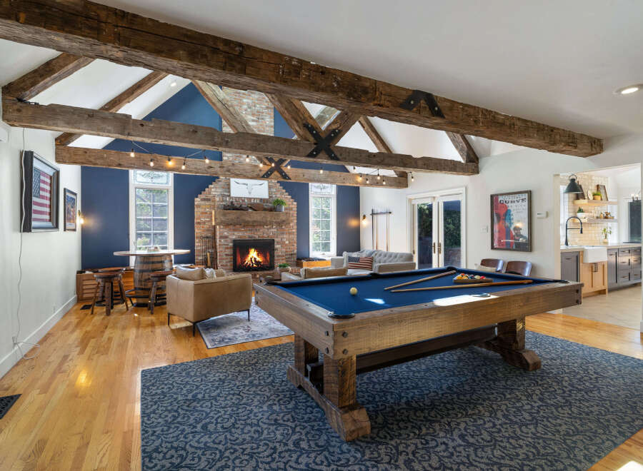 Experience rustic charm and modern entertainment in this spacious living area, featuring exposed wooden beams, a cozy brick fireplace, and a full-size pool table.