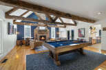 Experience rustic charm and modern entertainment in this spacious living area, featuring exposed wooden beams, a cozy brick fireplace, and a full-size pool table.