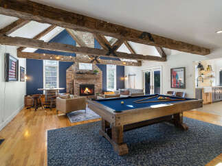 Experience rustic charm and modern entertainment in this spacious living area, featuring exposed wooden beams, a cozy brick fireplace, and a full-size pool table.