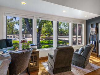 This home office offers a productive and relaxing atmosphere with a large desk, comfortable seating, and stunning views of the backyard oasis.