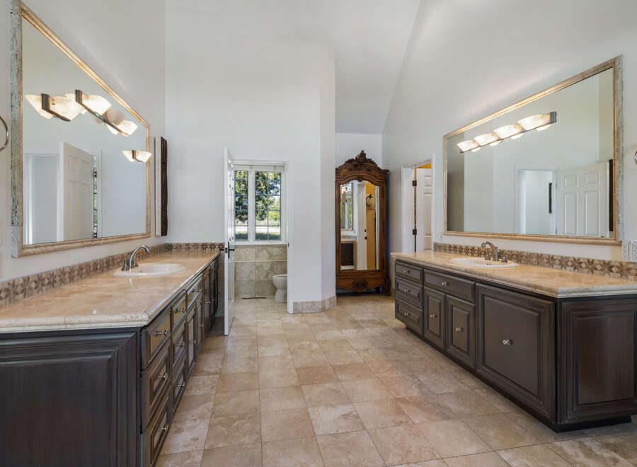 This spacious master bathroom features dual vanities with marble countertops and dark wood cabinetry, offering ample storage and a luxurious feel.