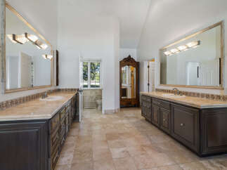 This spacious master bathroom features dual vanities with marble countertops and dark wood cabinetry, offering ample storage and a luxurious feel.