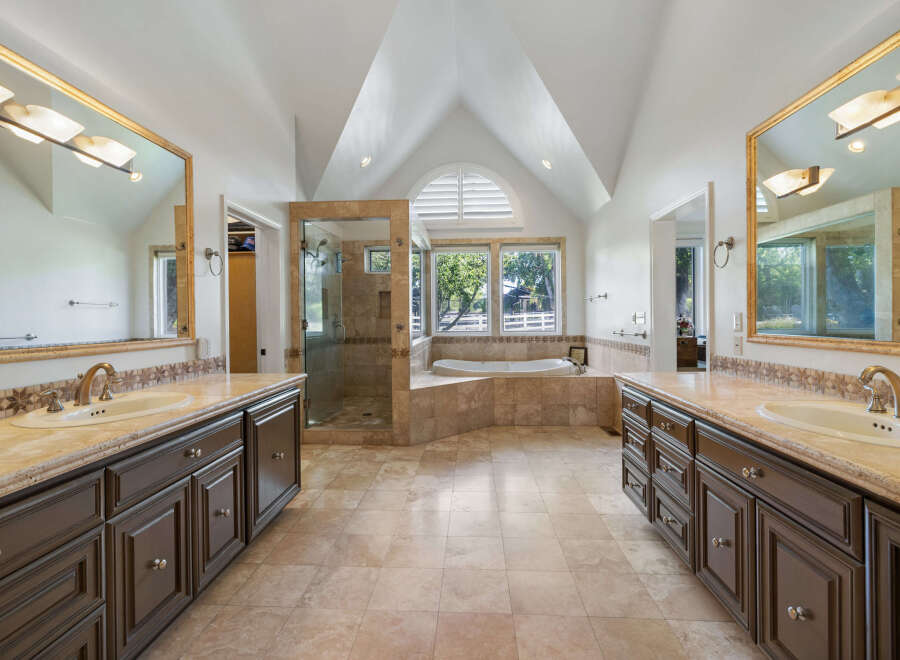 Experience luxury in this spacious master bathroom featuring dual vanities with granite countertops and dark wood cabinetry.