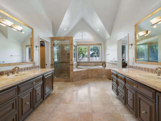 Experience luxury in this spacious master bathroom featuring dual vanities with granite countertops and dark wood cabinetry.