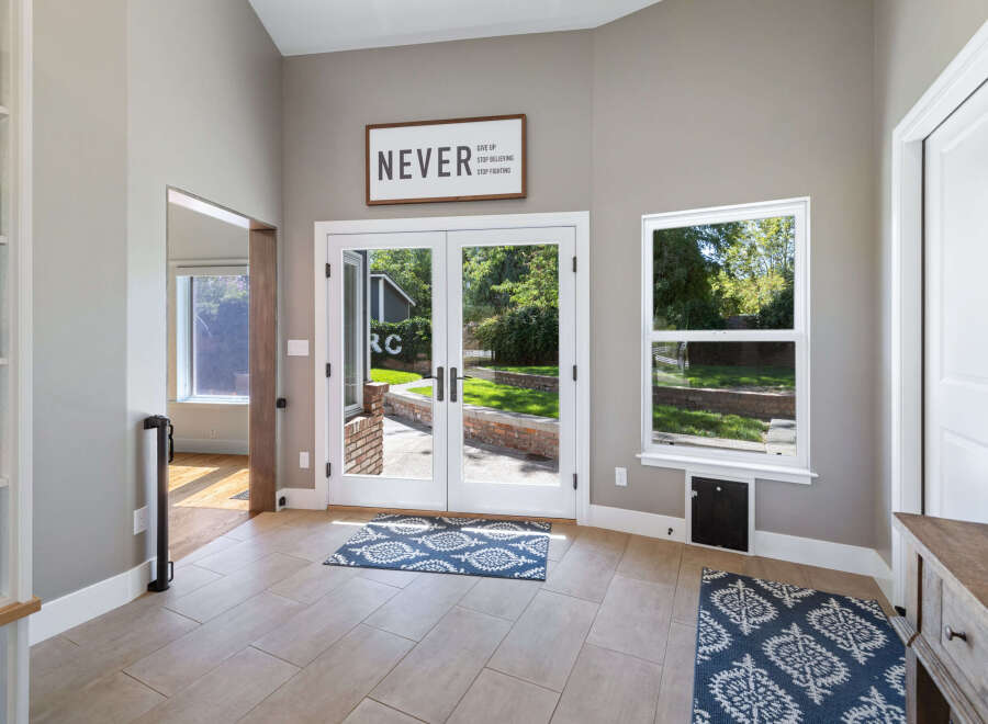 Step into this inviting entryway featuring a motivational 'Never Give Up' sign above elegant double doors that open to a lush backyard.