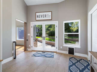 Step into this inviting entryway featuring a motivational 'Never Give Up' sign above elegant double doors that open to a lush backyard.