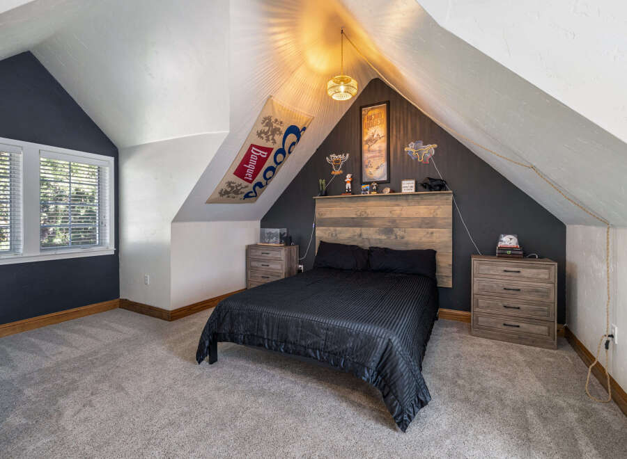Discover this unique attic bedroom featuring a cozy queen-size bed with a rustic wood headboard.