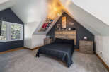 Discover this unique attic bedroom featuring a cozy queen-size bed with a rustic wood headboard.