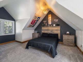 Discover this unique attic bedroom featuring a cozy queen-size bed with a rustic wood headboard.