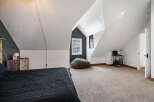 Discover this charming attic bedroom, featuring a cozy bed with a dark comforter and a rustic wooden nightstand.
