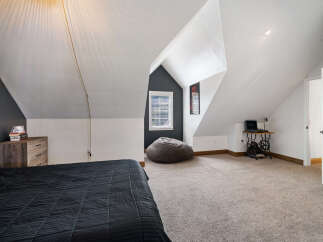 Discover this charming attic bedroom, featuring a cozy bed with a dark comforter and a rustic wooden nightstand.
