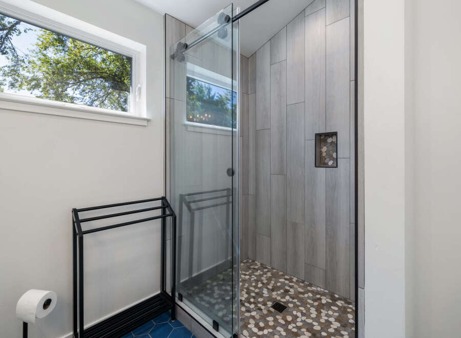 Experience modern luxury in this stunning bathroom, featuring a sleek glass-enclosed shower with unique pebble tile flooring and wood-look wall tiles.