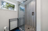 Experience modern luxury in this stunning bathroom, featuring a sleek glass-enclosed shower with unique pebble tile flooring and wood-look wall tiles.