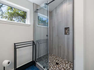 Experience modern luxury in this stunning bathroom, featuring a sleek glass-enclosed shower with unique pebble tile flooring and wood-look wall tiles.