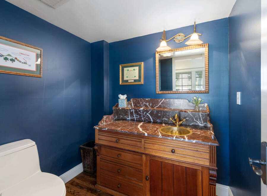 This powder room features a striking navy blue accent wall, complemented by a vintage-style wooden vanity with a marble countertop and a brass sink.