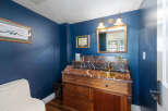 This powder room features a striking navy blue accent wall, complemented by a vintage-style wooden vanity with a marble countertop and a brass sink.