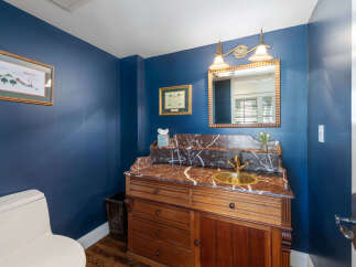 This powder room features a striking navy blue accent wall, complemented by a vintage-style wooden vanity with a marble countertop and a brass sink.