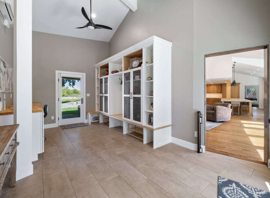 This spacious entryway features a large built-in white storage unit with glass-fronted cabinets and open shelving, perfect for organizing shoes and displaying decor.