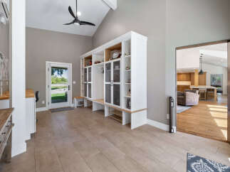 This spacious entryway features a large built-in white storage unit with glass-fronted cabinets and open shelving, perfect for organizing shoes and displaying decor.