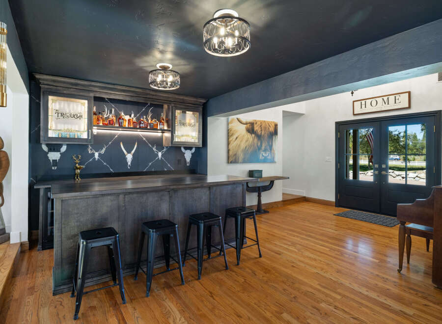Step into this stunning home bar, featuring a dark wood bar with ample seating and a backdrop of shelves stocked with liquor.