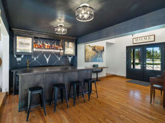 Step into this stunning home bar, featuring a dark wood bar with ample seating and a backdrop of shelves stocked with liquor.