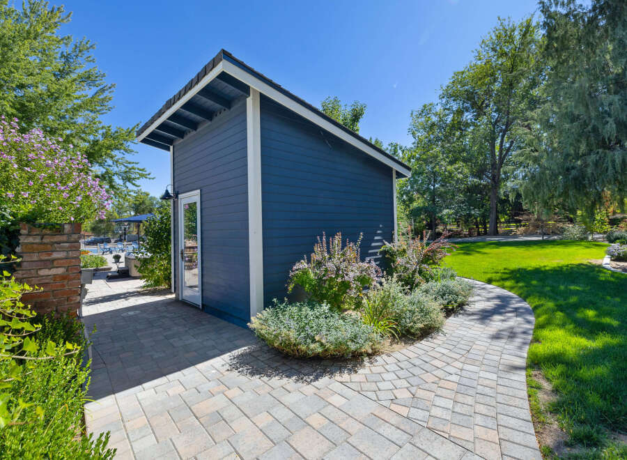 Discover this charming blue shed, perfect for storage or a backyard studio, nestled in a beautifully landscaped garden.