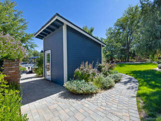 Discover this charming blue shed, perfect for storage or a backyard studio, nestled in a beautifully landscaped garden.