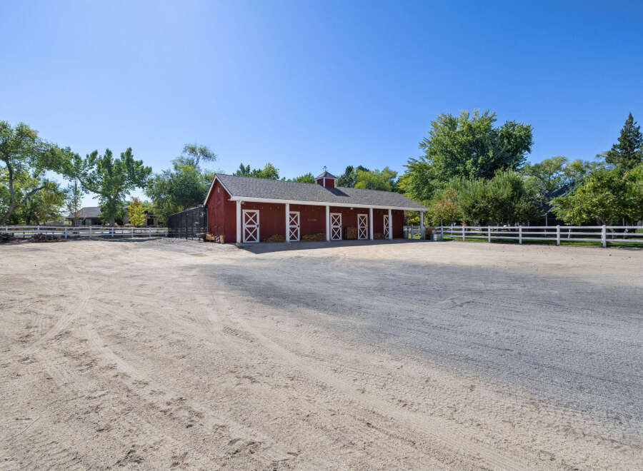 Discover this charming equestrian property featuring a classic red barn with multiple stalls and white cross-buck doors.